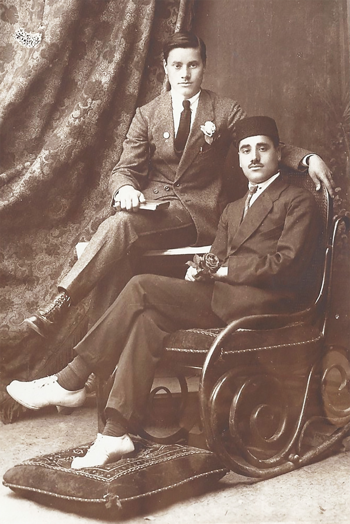 zwei Personen sitzend auf Lehnstuhl vor Wandteppich